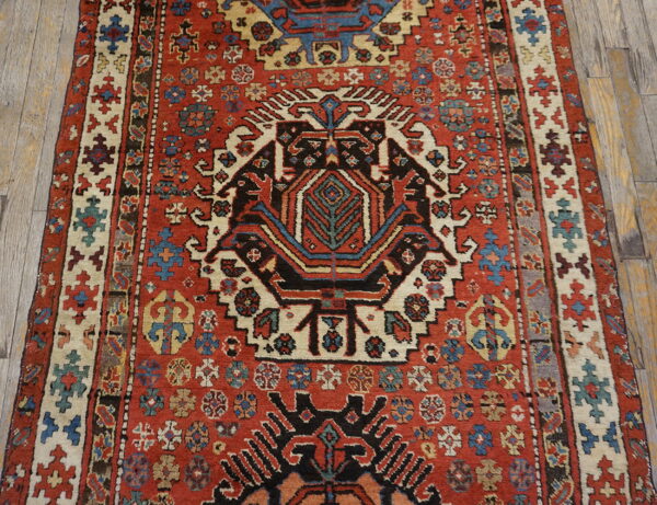Rust red geometric rug with a black and cream central medallion rests on rustic wooden floors.