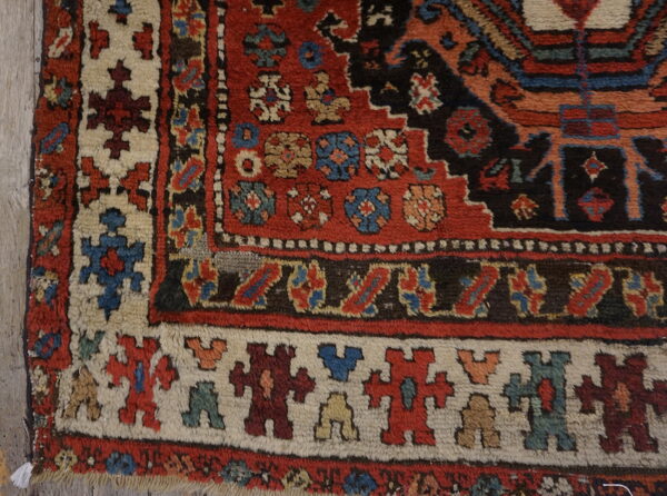 A highly patterned rug corner shows red, dark blue, and cream geometric motifs on light wood flooring.