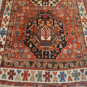 Close-up of a rustic geometric rug in rust, black, and cream with a stylized figure border on light wood flooring.