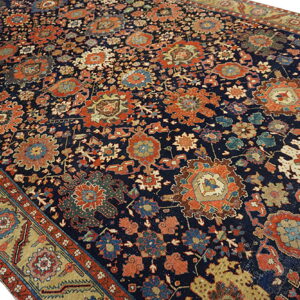 Dark blue rug with dense traditional patterns in rust, gold, and teal, featuring a wide gold border.