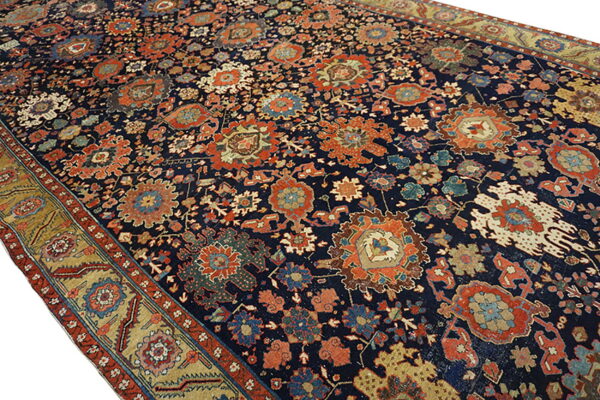 Dark blue rug with dense traditional patterns in rust, gold, and teal, featuring a wide gold border.