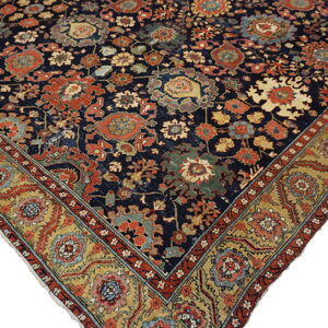 Ornate rug corner featuring a dark blue field, detailed red, gold, and teal floral motifs, and an ochre border.