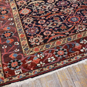 A low-pile rug with a navy floral field and wide reddish-brown borders rests on distressed wood flooring.