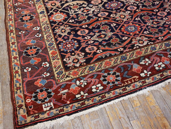 A low-pile rug with a navy floral field and wide reddish-brown borders rests on distressed wood flooring.