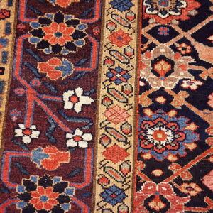 Deeply colored traditional rug detail featuring red, navy, tan, and blue geometric and floral designs near wood floor.