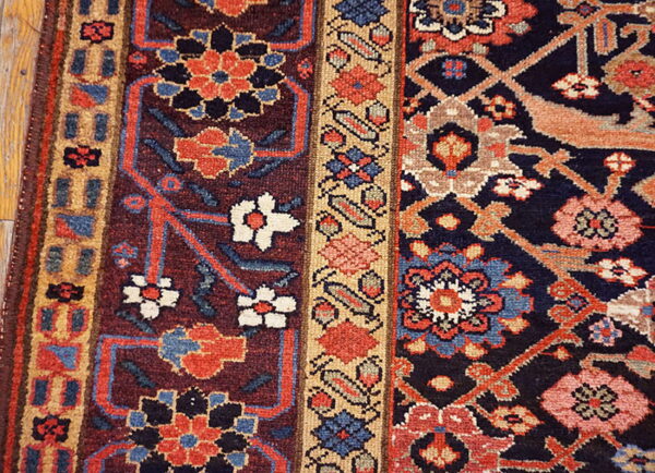Deeply colored traditional rug detail featuring red, navy, tan, and blue geometric and floral designs near wood floor.