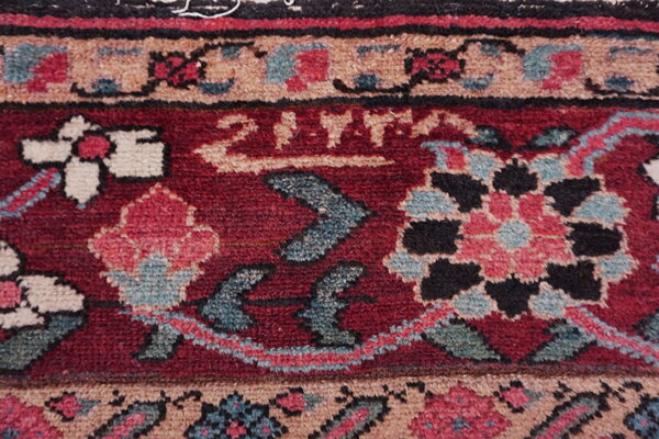 Detailed view of a low pile rug featuring red, tan, teal, and pink stylized floral and geometric motifs.