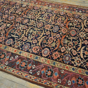 Low-pile rug with a detailed navy blue field and rust border featuring complex floral motifs on wood flooring.