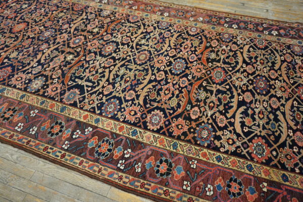 Low-pile rug with a detailed navy blue field and rust border featuring complex floral motifs on wood flooring.