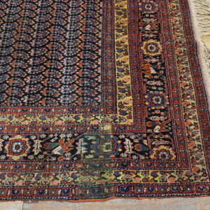 Dark blue rug with complex geometric patterns, red border, and fringe detail rests on hardwood planks.