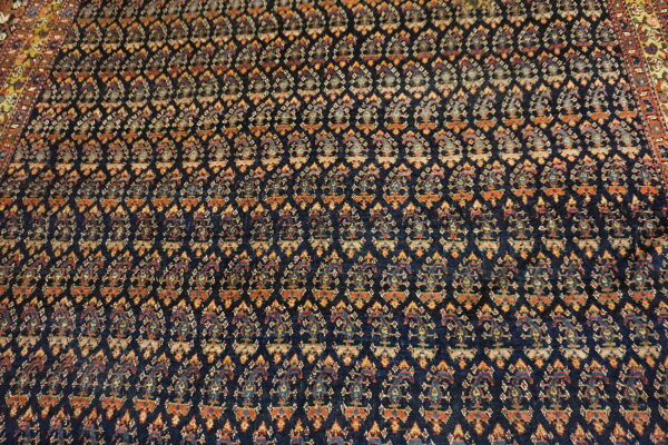 Dark blue rug with repeating traditional boteh patterns in rust, gold, and light blue accents.