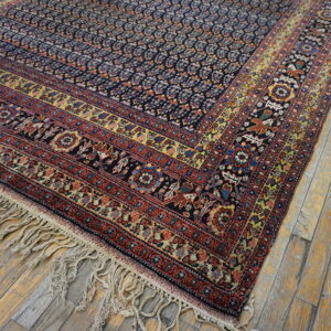 A densely patterned rug with red, gold, and navy borders rests on worn, light-colored wood floor planks.