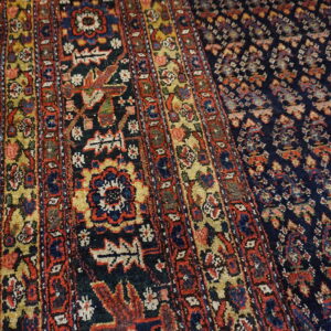 Low-pile traditional rug featuring dense geometric patterns in navy, red, and gold colors near light wood.
