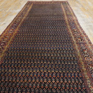 Long, low-pile runner rug with a navy field and repeating gold/rust motifs on light hardwood planks.