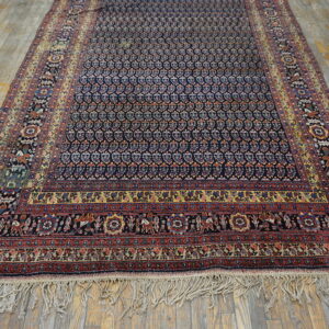 Navy rug with detailed red, yellow, and blue borders lies on distressed wide plank hardwood flooring.