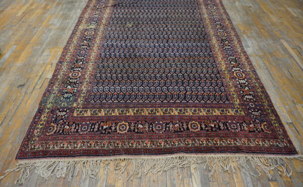 Navy rug with detailed red, yellow, and blue borders lies on distressed wide plank hardwood flooring.