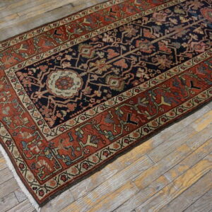 Traditional navy and terracotta runner rug with intricate patterns lies angled on distressed wood plank flooring.