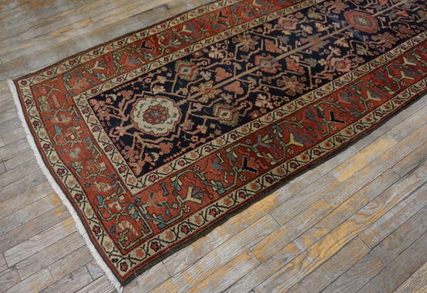 Traditional navy and terracotta runner rug with intricate patterns lies angled on distressed wood plank flooring.