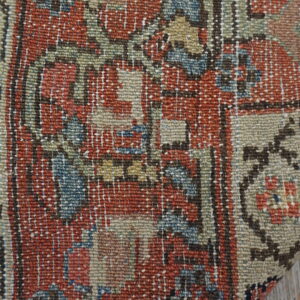 Close-up of a low-pile rug with rust, beige, and blue pattern, white fringe, on plank flooring.