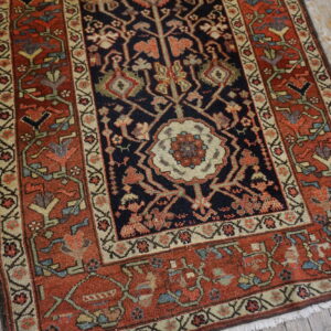 Ornate traditional rug with dark center and rust border rests on distressed light wood plank flooring.