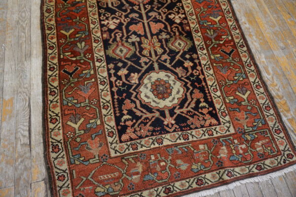 Ornate traditional rug with dark center and rust border rests on distressed light wood plank flooring.