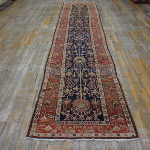 A long, navy and rust traditional runner rug lies centered on distressed wooden floorboards.