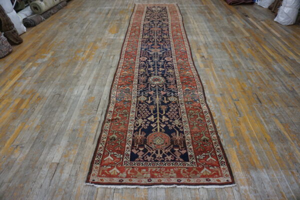 A long, navy and rust traditional runner rug lies centered on distressed wooden floorboards.