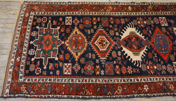 Geometric high-pile runner rug in navy and rust with colorful medallions, displayed on light wood floorboards.