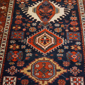 Traditional geometric rug in navy blue, rust red, and cream on light wood flooring.