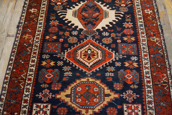 Traditional geometric rug in navy blue, rust red, and cream on light wood flooring.