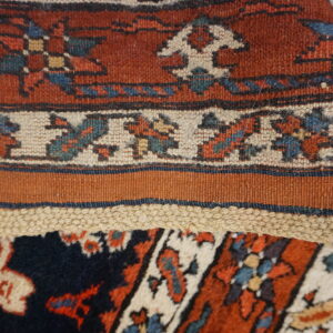 A folded rug displays rust high pile knotting, a cream patterned border, and a flatwoven edge.