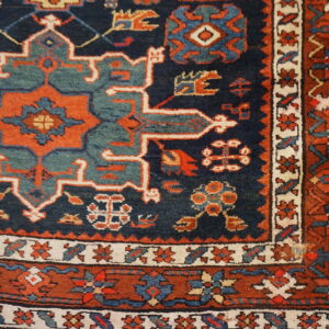 Geometric patterned rug corner in deep blue, rust, and dusty teal on light wooden flooring.