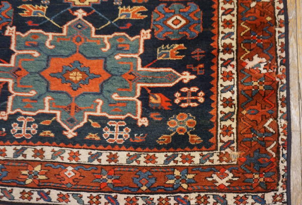 Geometric patterned rug corner in deep blue, rust, and dusty teal on light wooden flooring.