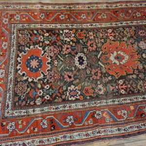 Low-pile rug with complex red, blue, cream, and brown traditional patterns on plank wood flooring.