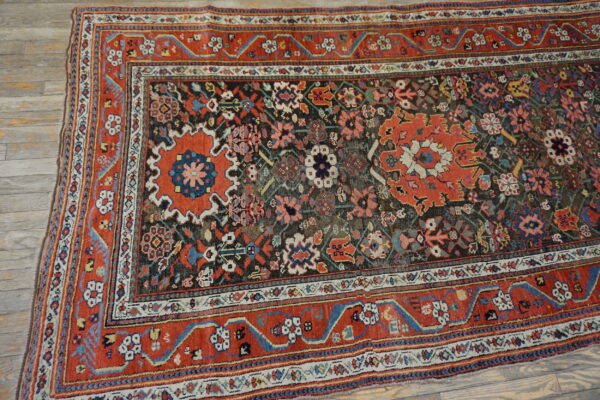 Low-pile rug with complex red, blue, cream, and brown traditional patterns on plank wood flooring.