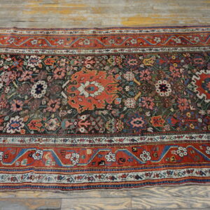 Multi-colored patterned rug with a dark center field and wide red border rests on weathered wooden planks.