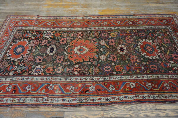 Multi-colored patterned rug with a dark center field and wide red border rests on weathered wooden planks.