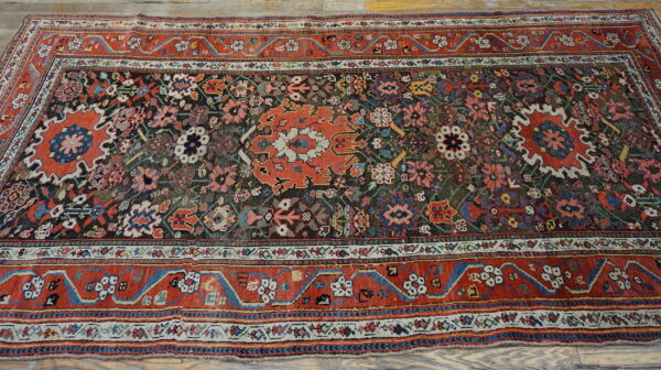 Intricate floral rug with a rust-red border and dark field, displayed on gray wood flooring.