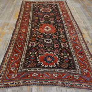 Red and black traditional runner rug with floral medallions rests on distressed, light gray wood floors.