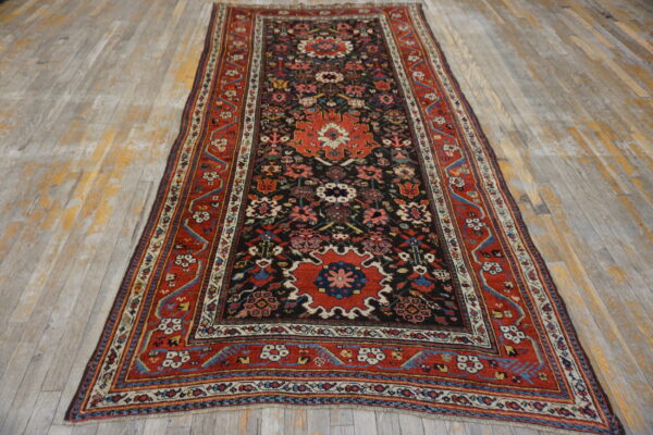 Red and black traditional runner rug with floral medallions rests on distressed, light gray wood floors.