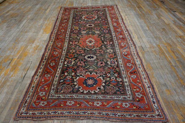 Intricate red, dark blue, and cream runner rug displayed on distressed light gray and yellow wood planks.