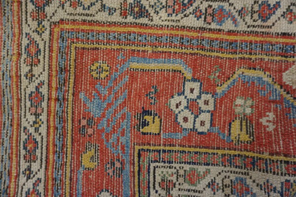 Woven rug detail showing a rust-red field, cream border, and complex blue and yellow patterns.
