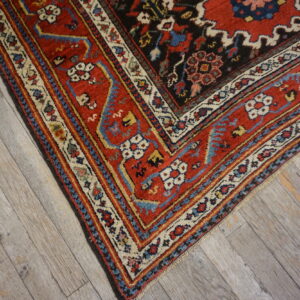 Detailed corner of a red and blue patterned rug resting on weathered gray wood flooring.