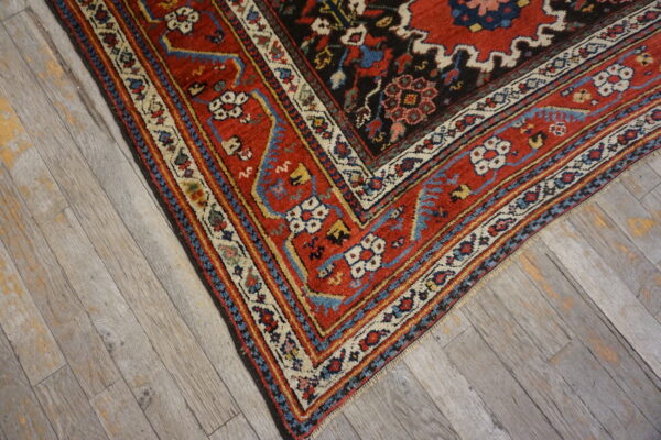 Detailed corner of a red and blue patterned rug resting on weathered gray wood flooring.