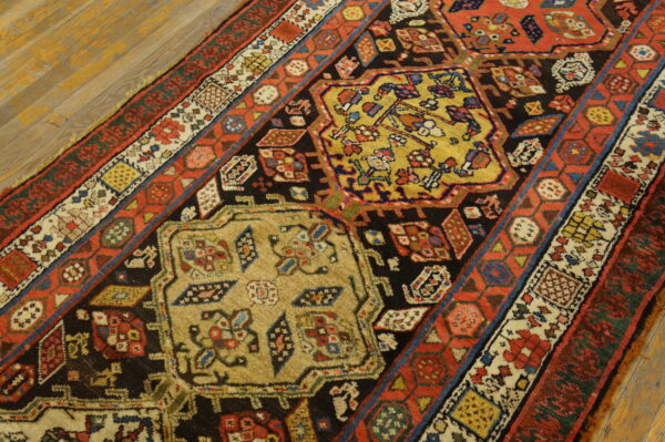 Multicolored traditional rug with detailed yellow, red, and black geometric designs rests on light wood flooring.