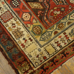 Thick pile rug corner with complex red, cream, teal, and brown borders resting on weathered wood planks.