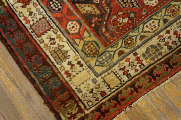 Thick pile rug corner with complex red, cream, teal, and brown borders resting on weathered wood planks.