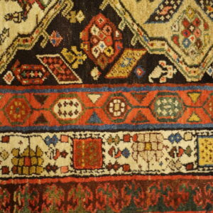 This medium-pile rug detail shows red, beige, and black geometric bands accented by blue and yellow motifs.