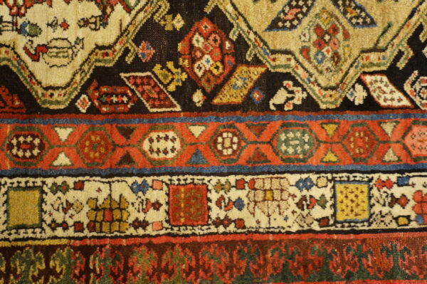 This medium-pile rug detail shows red, beige, and black geometric bands accented by blue and yellow motifs.