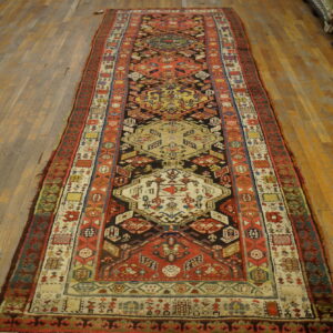 Geometric runner rug in red, black, and cream on worn light brown wood floors.